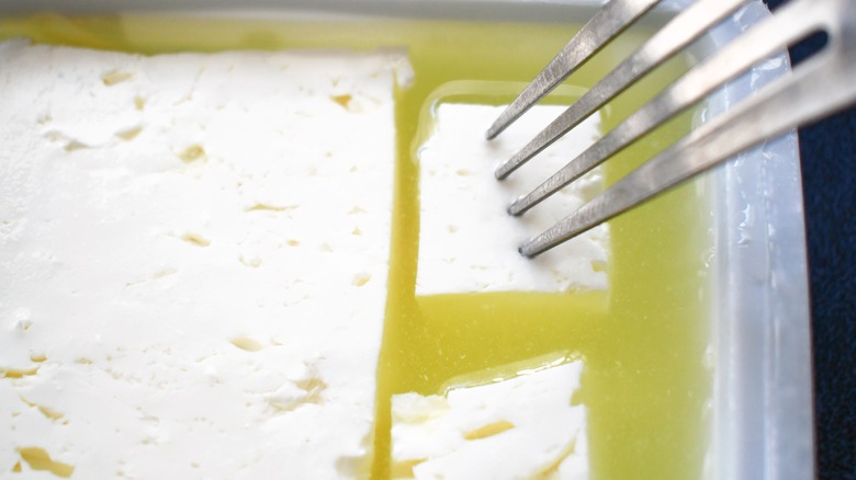 Fork poking feta block in brine