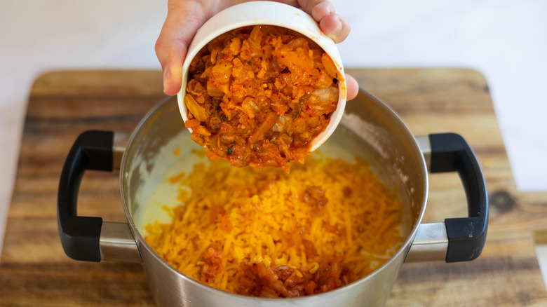 Hand pouring kimchi in mac and cheese pot