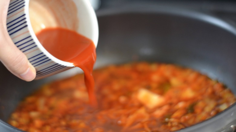 pouring red condiment into pot