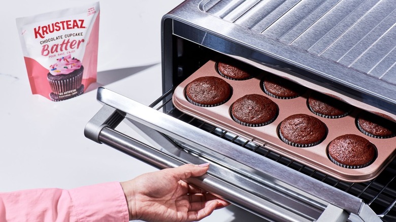 Person removing pan of fresh-baked chocolate cupcakes from oven