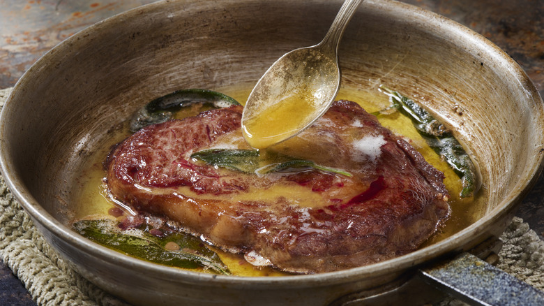 spoon basting steak with butter and sage