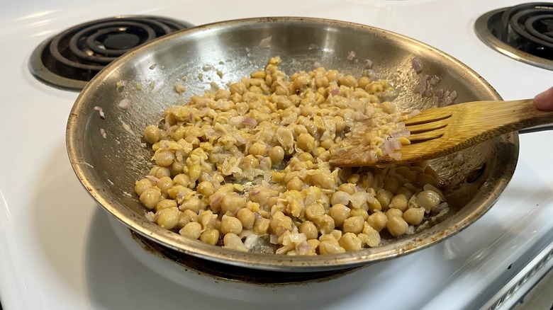 wooden spoon mashing chickpeas in a skillet