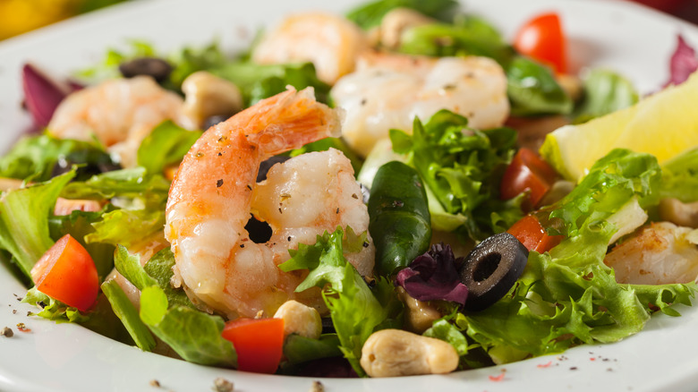 A salad with shrimp, lettuce, cherry tomatoes, cashew, and olives