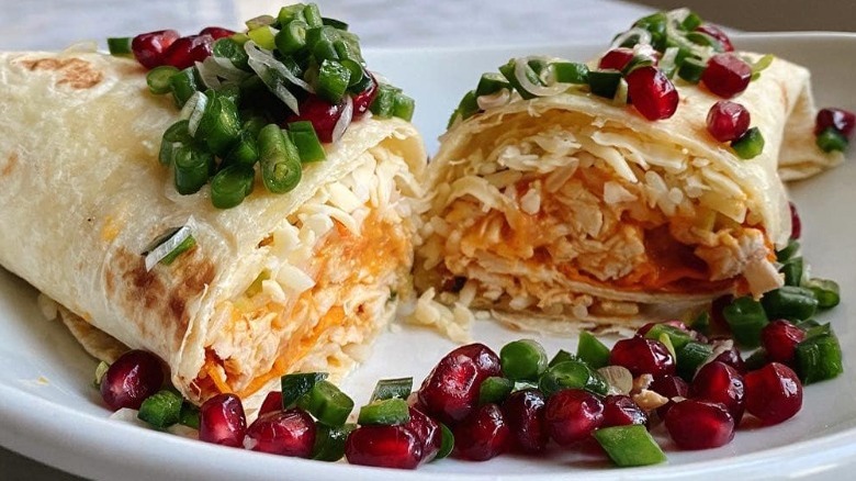 burrito filled with rice and topped with greens and pomegranetes