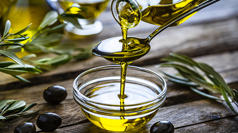 Olive oil pouring into spoon and glass bowl