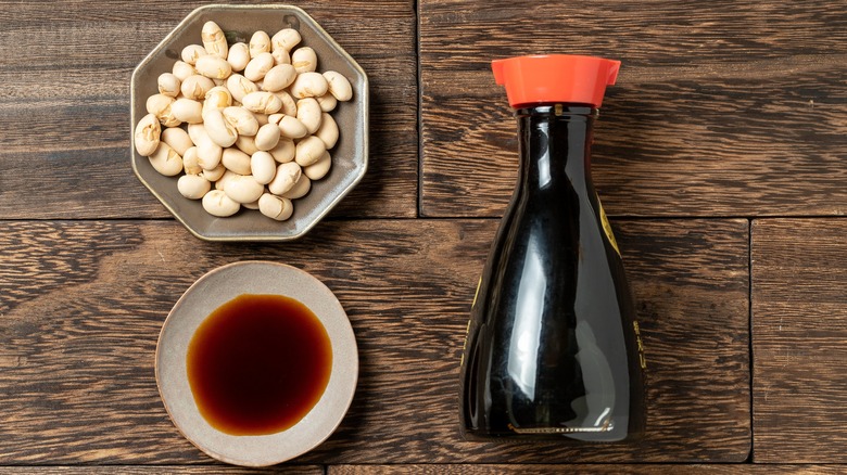 Soy sauce bottle and ramekin of soy beans on wood table