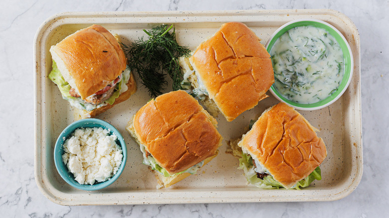 A baking sheet with four sliders, feta and tzatziki sauce