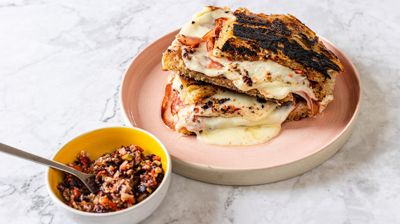 Side view of two slices of gooey, melty grilled cheese besides giardiniera spread