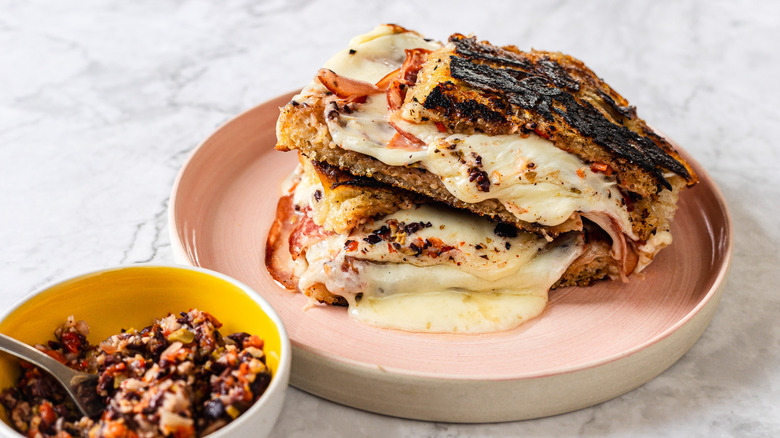 Side view of two slices of gooey, melty grilled cheese besides giardiniera spread