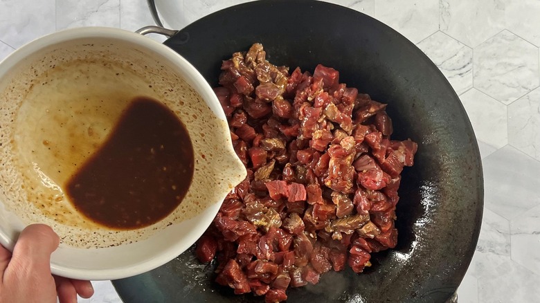 hand pouring marinade in pan of steak