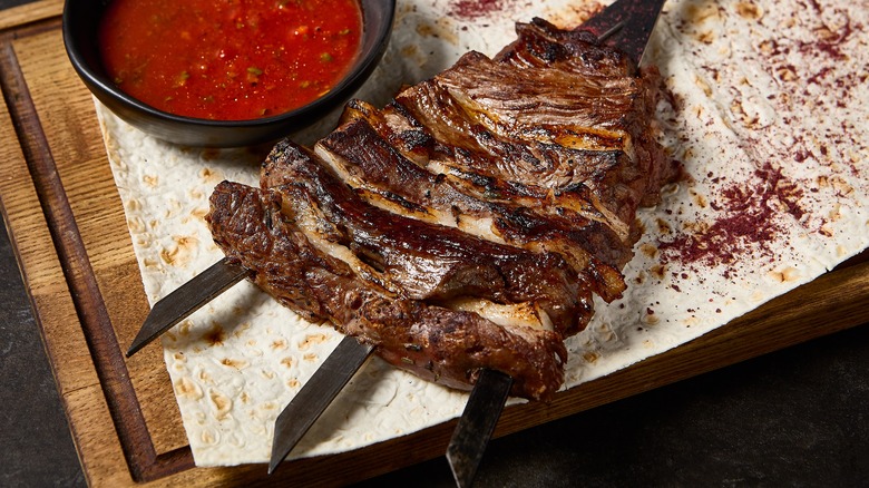 Grilled lamb breast on a skewer next to red sauce