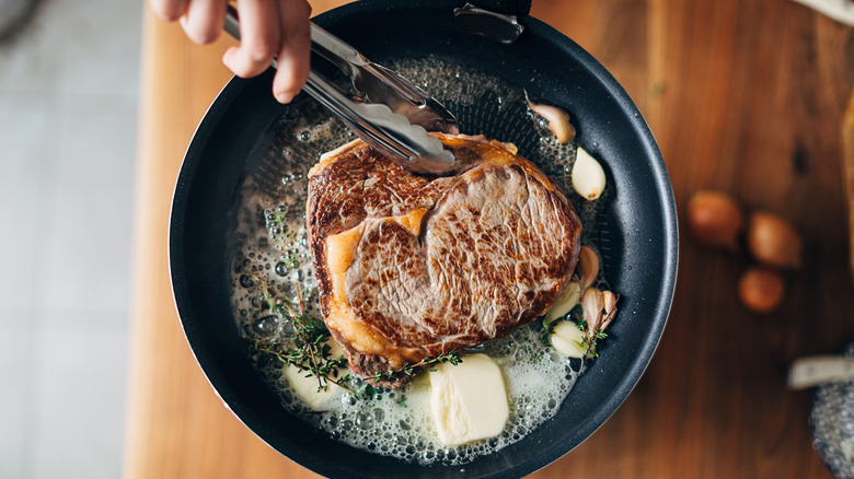 Overhead shot of chef preparing ribeye with butter, thyme and garlic.