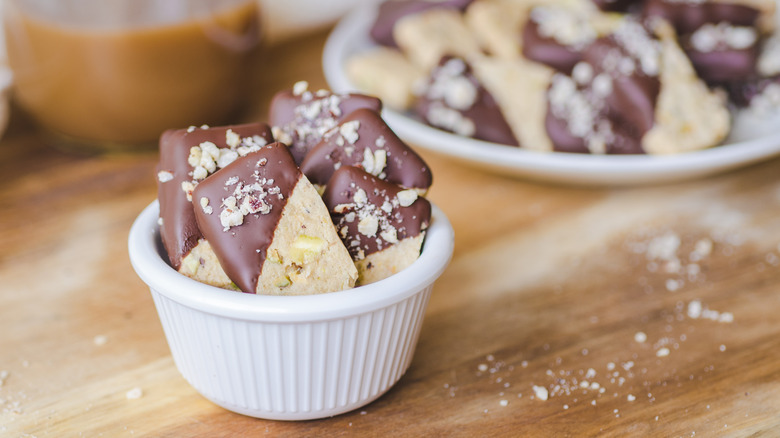 A close up shot of chocolate dipped crunchy buttery hazelnut pistachio shortbread mini cookies sprinkled with nuts