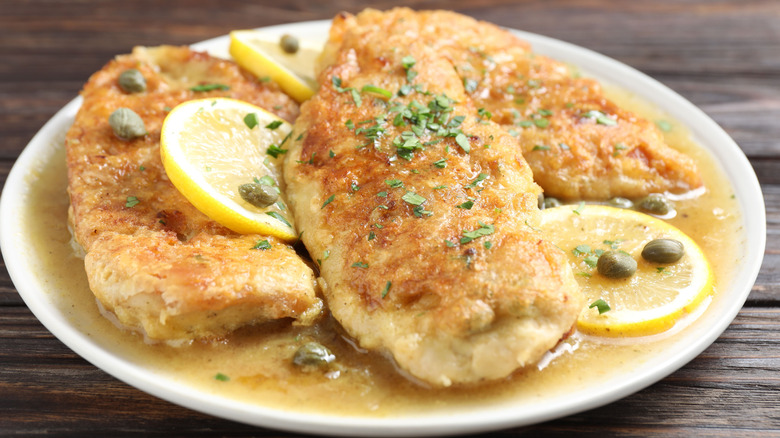 chicken piccata on white plate atop wooden table, closeup