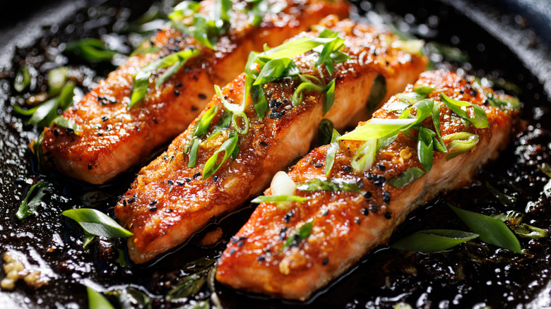 Honey miso salmon filets sprinkled chopped scallion in a black baking dish, focus on the middle, close up view