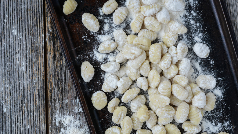 uncooked gnocchi on cookie sheet atop rustic wood table