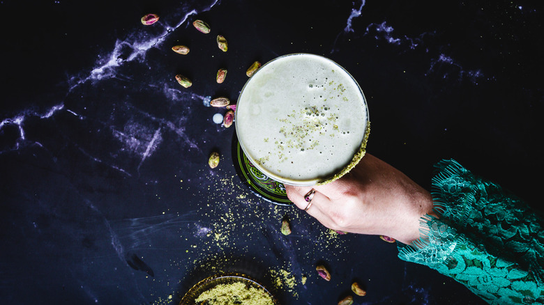 Hand holding a pistachio martini against a black marble background.