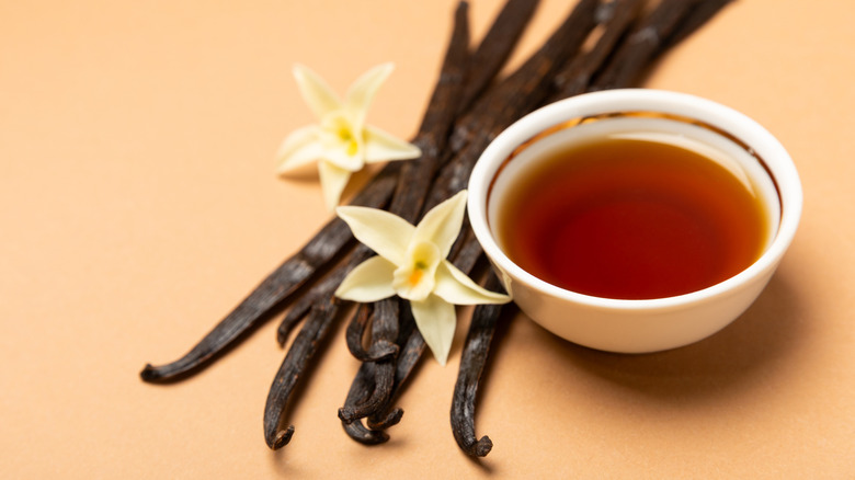A small bowl of vanilla extract next to vanilla beans