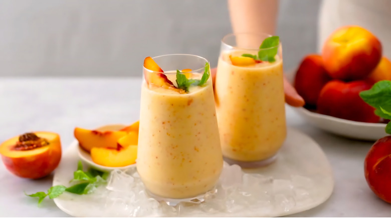 Two thick peach smoothies with mint on a plate of ice