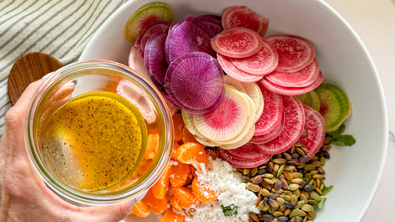 hand adding dressing to bowl