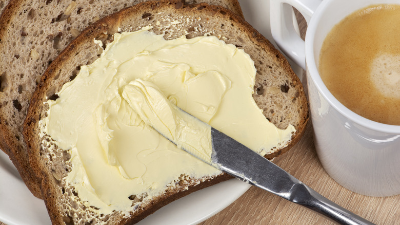 margarine spread with knife on piece of bread next to cup of tea 