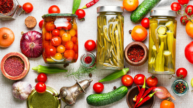 different vegetables, spices, herbs, and marinated vegetables in jars on a white background