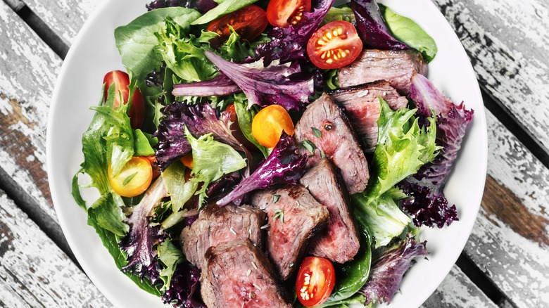 sliced steak over salad on a white table