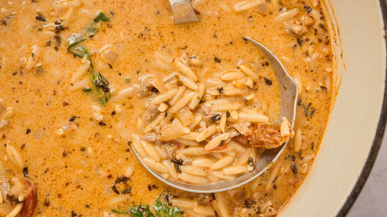 A ladle scooping out orzo soup from a pot