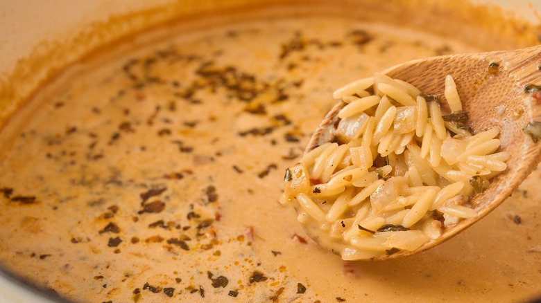 A spoon scooping out al dente orzo from a pot of soup