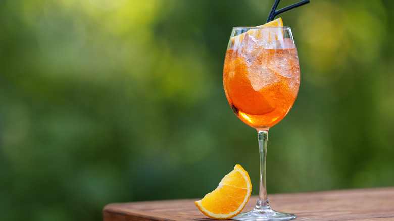 A glass of sparkling Aperol with a wedge of orange beside it
