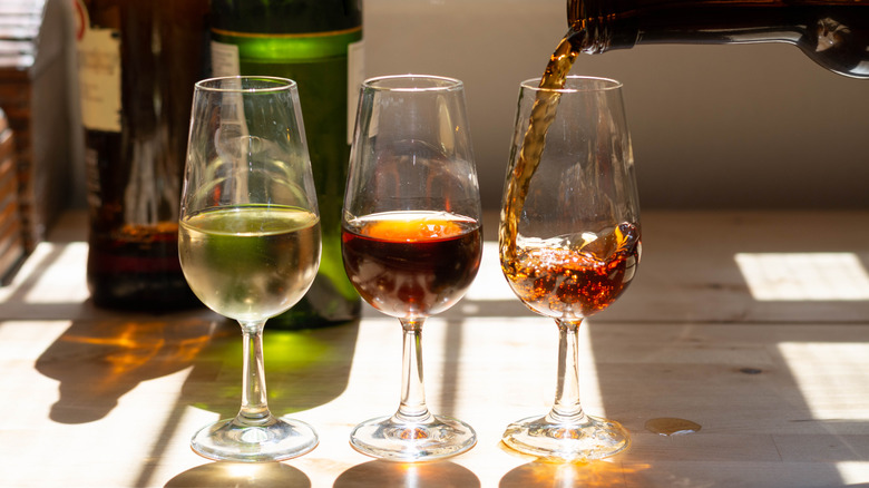 Three glasses of different sherries, with a bottle pouring into one