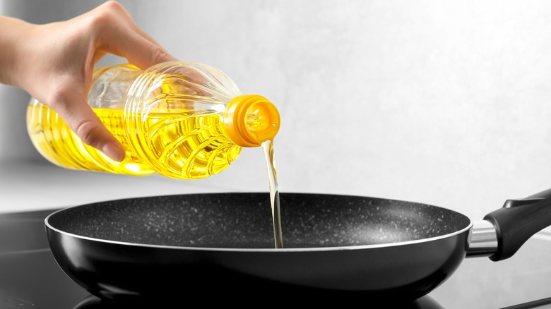 Hand pouring oil into skillet