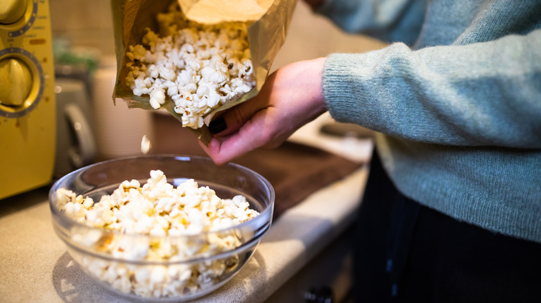 Hand pouring microwaved popcorn into bowl