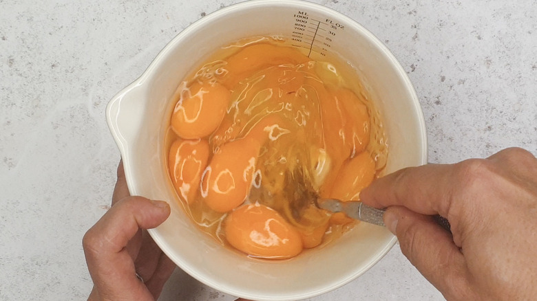 Hands whisking eggs in measuring cup