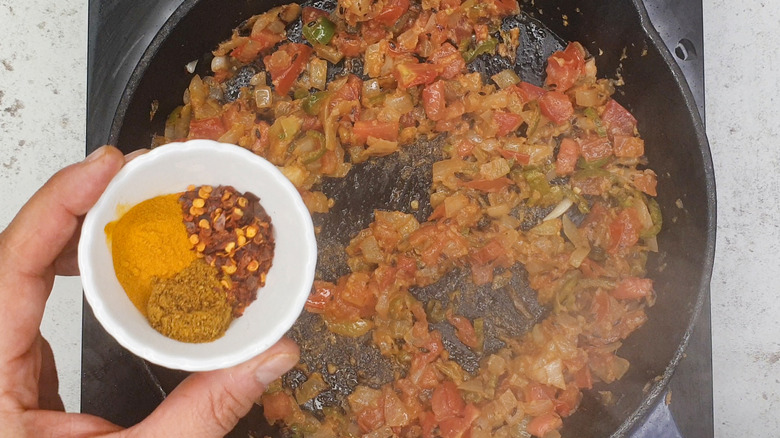 Hand adding spices to pan of tomato mixture