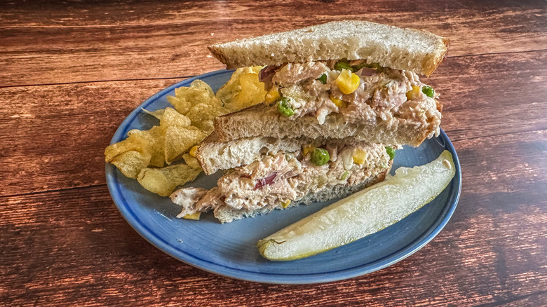 tuna fish salad sandwich with chips and a pickle