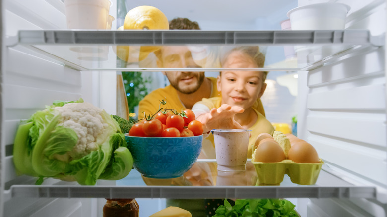 A child reaches for food inside a fridge.