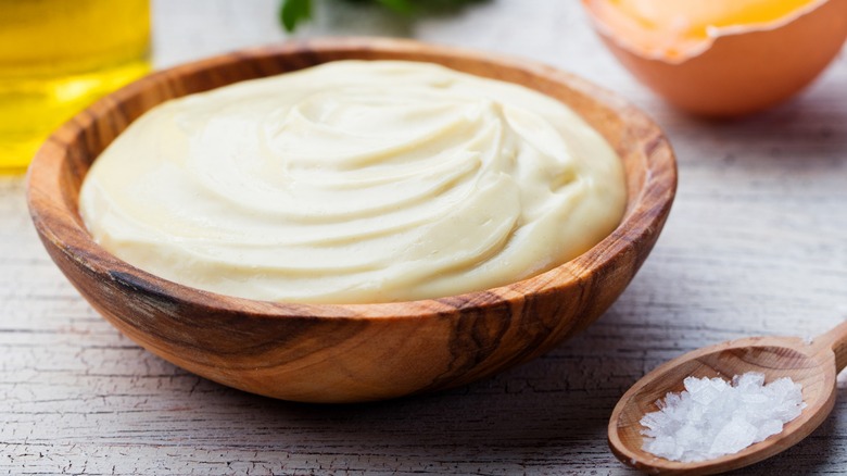 Wooden bowl of mayonnaise next to a spoon of salt