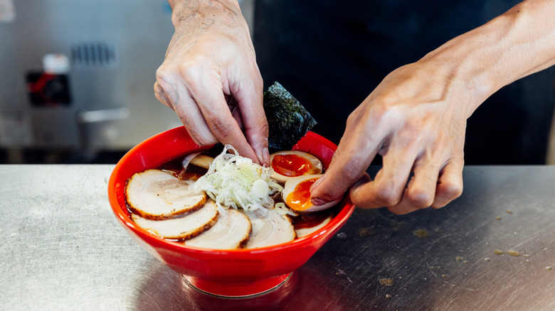 chef's hands assembling bowl of ramen