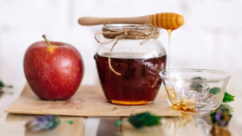 An apple next to a jar and bowl of honey