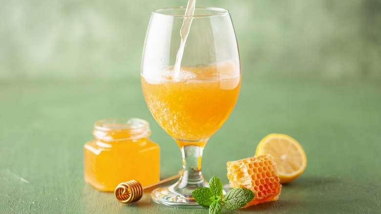 A glass of mead being poured next to honey