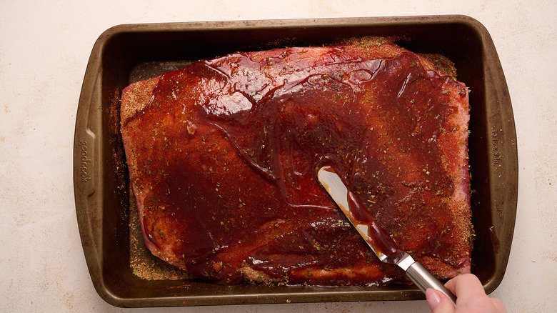 Spreading barbecue sauce on brisket