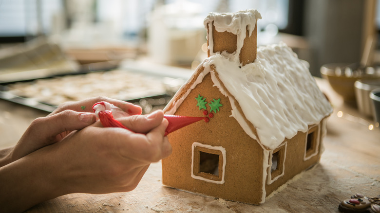 Hands piping icing onto gingerbread house