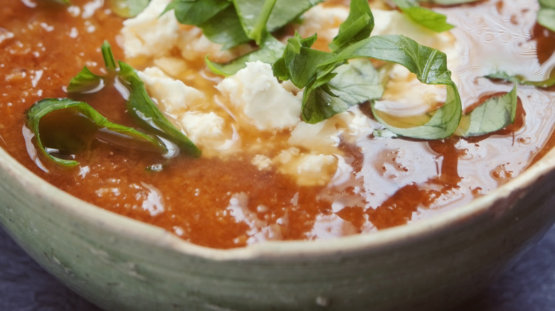 Close-up of tomato soup with crumbled feta and torn fresh basil