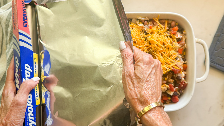 hands covering dish with foil