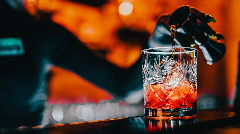 A bartender pouring a mixer into a Negroni