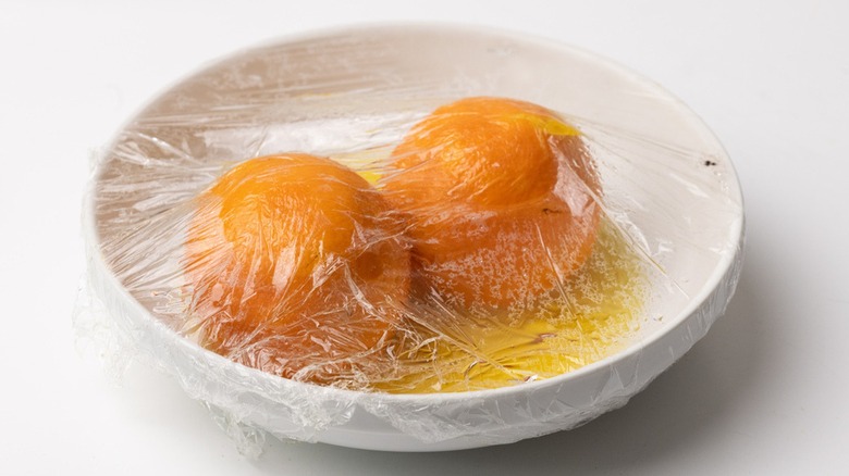 Oranges on plate with plastic wrap 