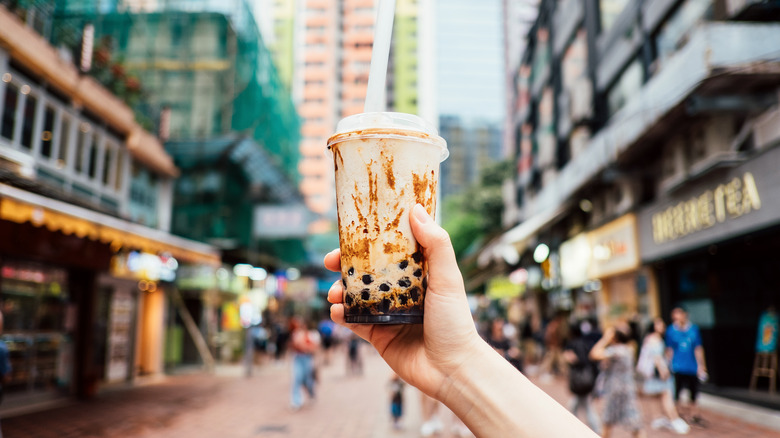 Person holding a brown sugar boba tea in an outdoor street setting