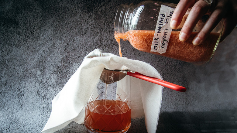 Pouring Negroni from jar through strainer