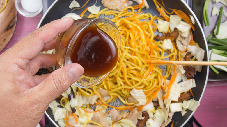 Person pouring sauce on noodles